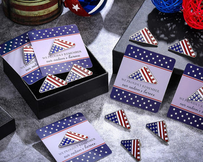 Patriotic-themed enamel pins and matching cards displayed in a black gift box on a gray textured surface, with decorative balls and woven balls in the background.